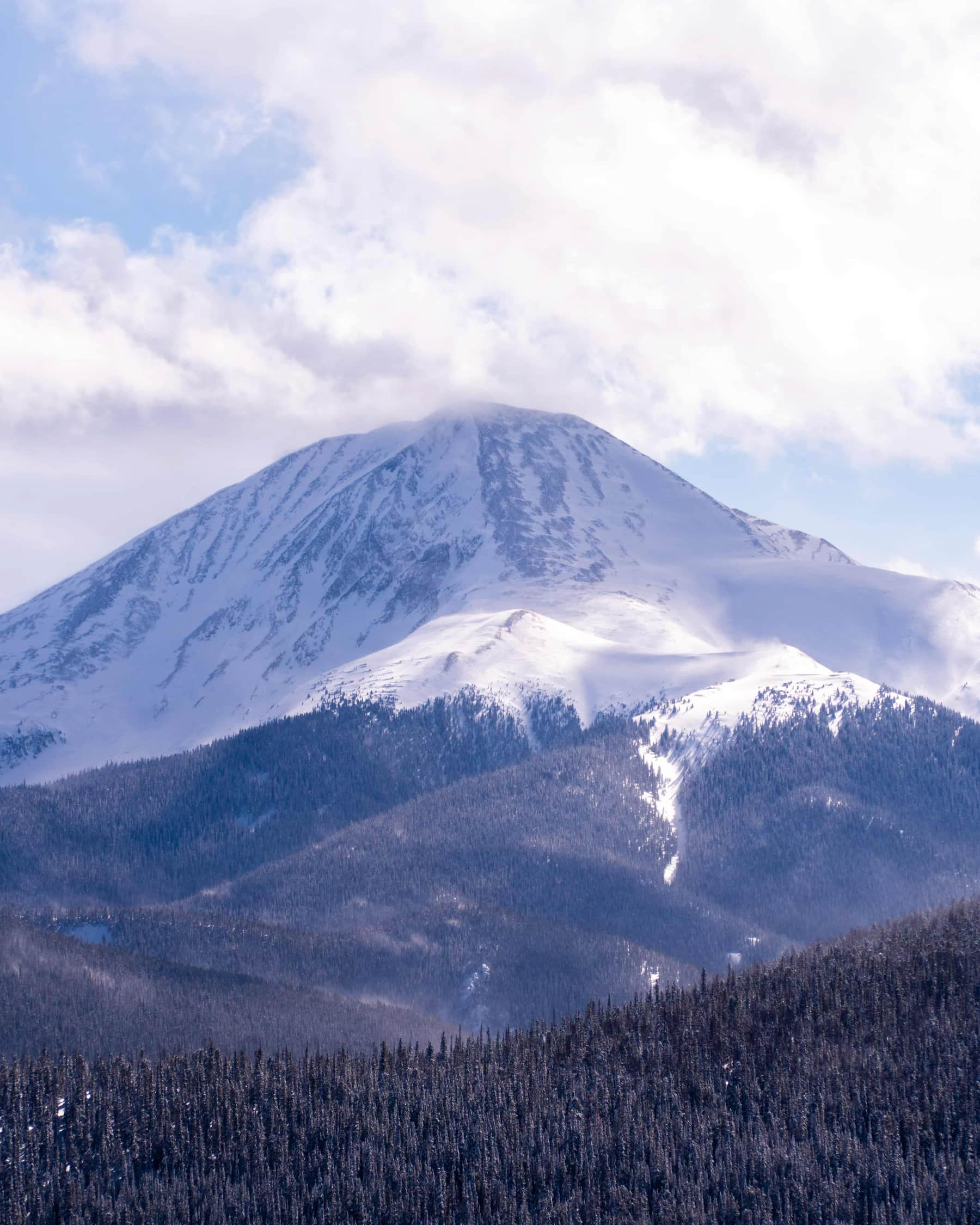 A mountain with a snow cap and clouds above